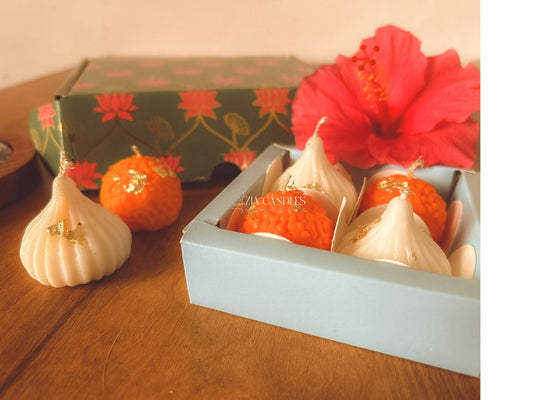 Ganpati festive gift set featuring handcrafted 100% soy wax ladoo candles and modak candles with gold foil, in a lotus-print decorative box for pooja décor and gifting.